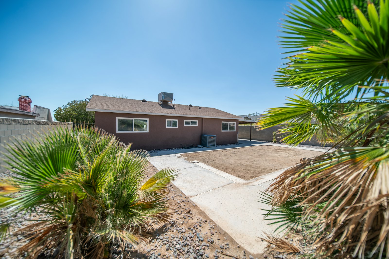 Phoenix-area home with a large fan palm and freshly-edged gravel beds along the driveway.